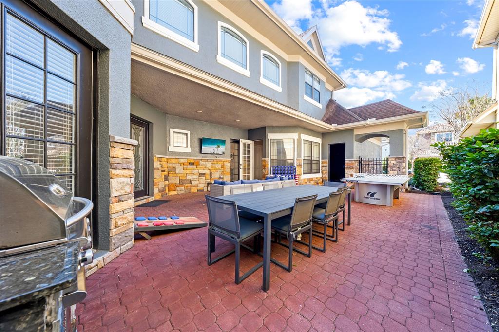 A paved patio features a dining table, outdoor seating, a grill, and a ping pong table — 785 GOLDEN BEAR DRIVE, REUNION, FL
