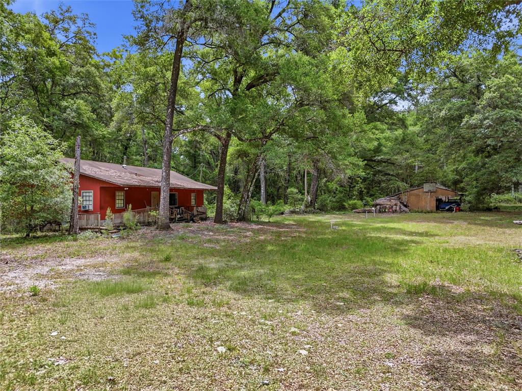 A red house with a wooden deck sits on a grassy lot near trees — 8009 SW 131ST TERRACE, ARCHER, FL