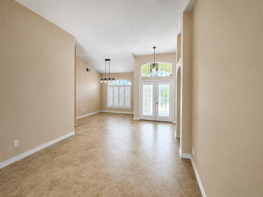 An open-concept dining area features tile flooring, a vaulted ceiling, and double glass entry doors — 8032 PINE HOLLOW DRIVE, MOUNT DORA, FL