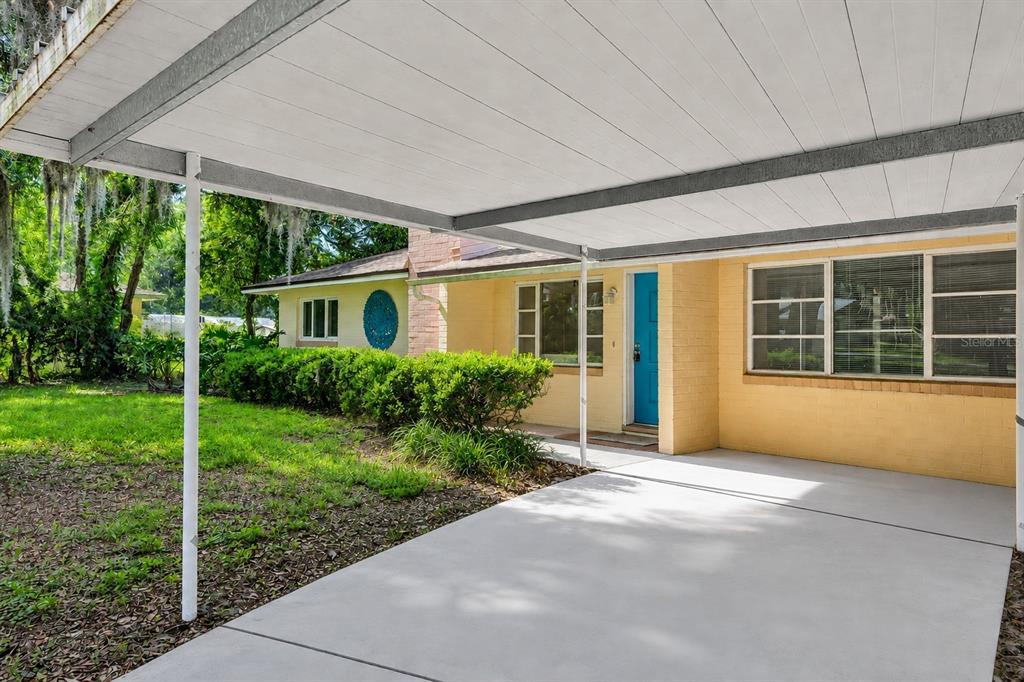 A concrete carport leads to the front entrance of a yellow brick house — 1503 MOSS AVENUE, LEESBURG, FL