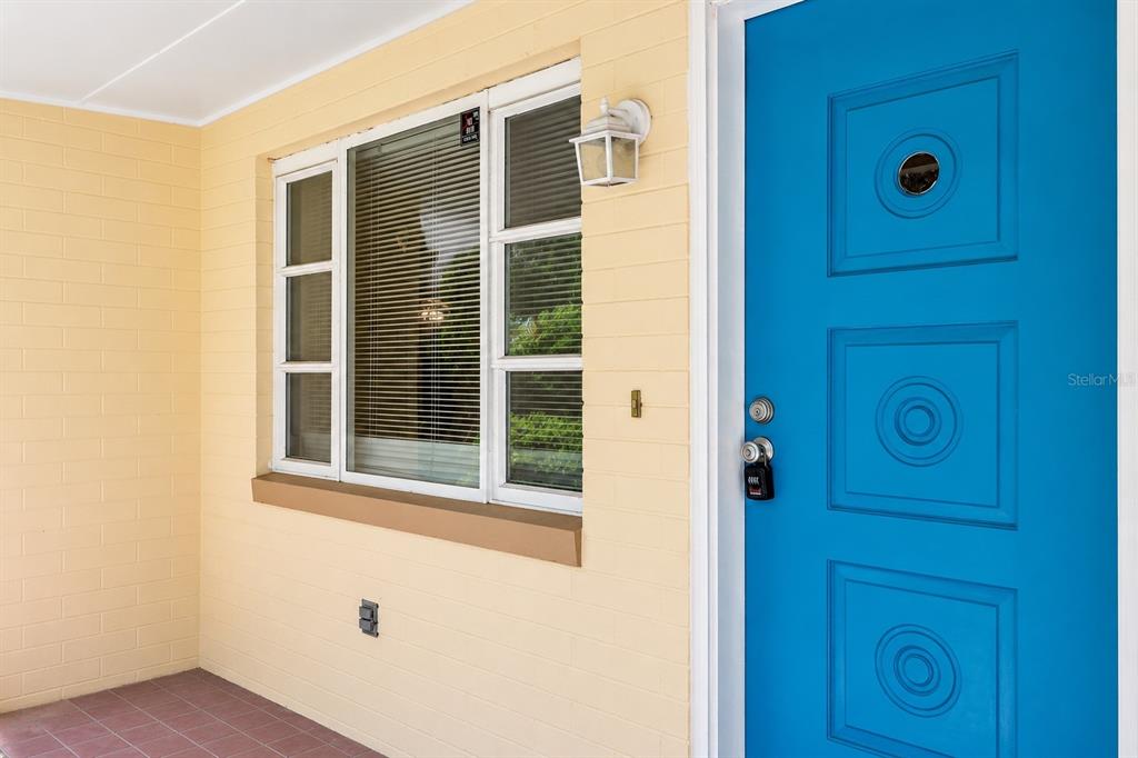 A bright blue front door sits next to a window on a yellow brick porch — 1503 MOSS AVENUE, LEESBURG, FL