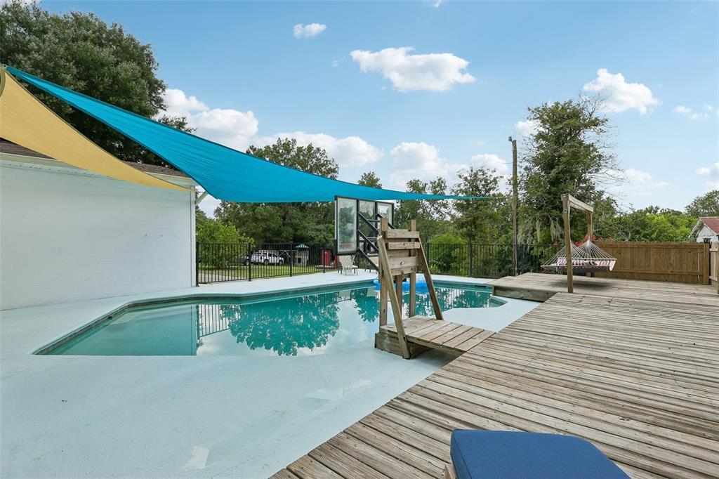 A swimming pool with a wooden deck, basketball hoop, and blue shade sail outdoors — 8904 CLAYTON LANE, LAKELAND, FL