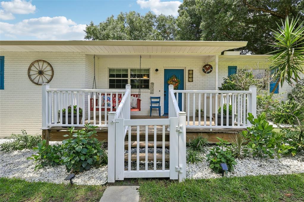A white brick house features a wooden front porch with a white railing and gate — 8904 CLAYTON LANE, LAKELAND, FL