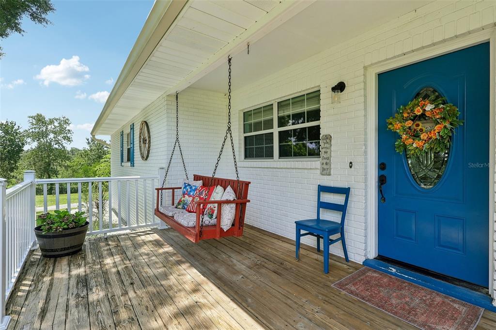 A wooden porch features a red hanging swing, a blue chair, and a blue door — 8904 CLAYTON LANE, LAKELAND, FL