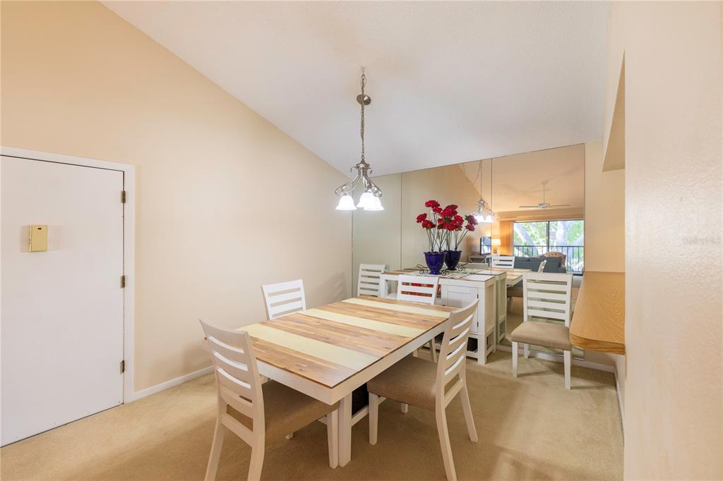 A dining room features a wooden table, white chairs, a vaulted ceiling, and mirrored walls — 646 BIRD BAY DRIVE E UNIT 207, VENICE, FL