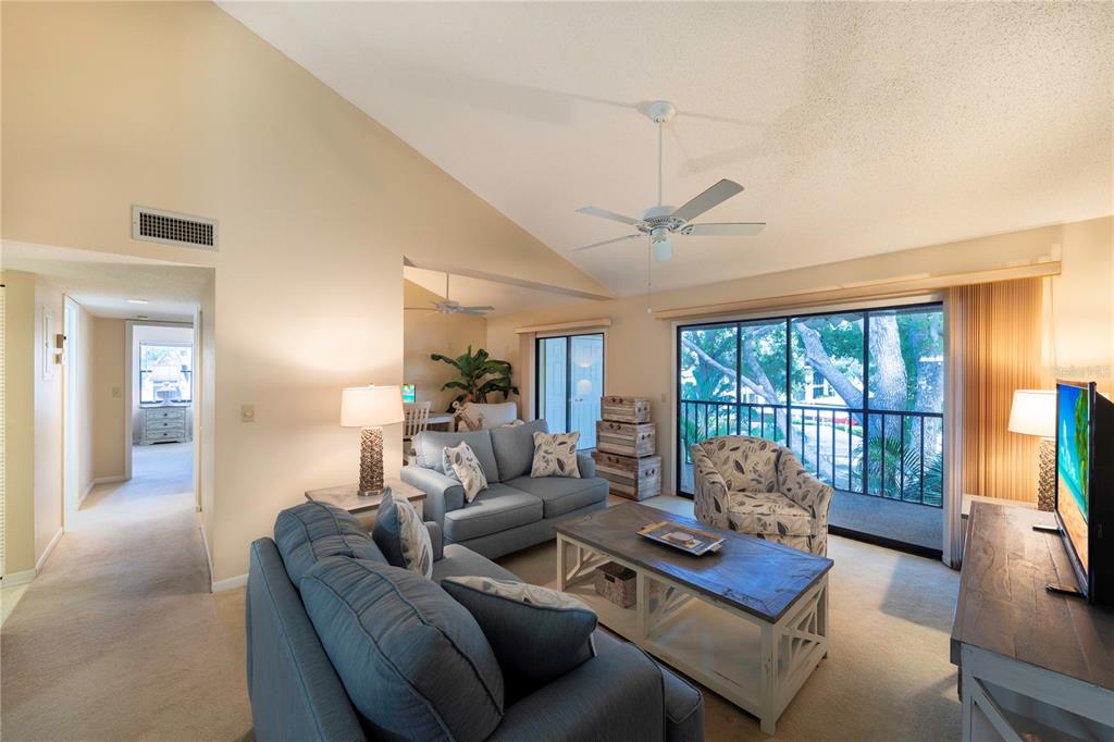 A living room features blue sofas, a wooden coffee table, and a sliding glass door — 646 BIRD BAY DRIVE E UNIT 207, VENICE, FL