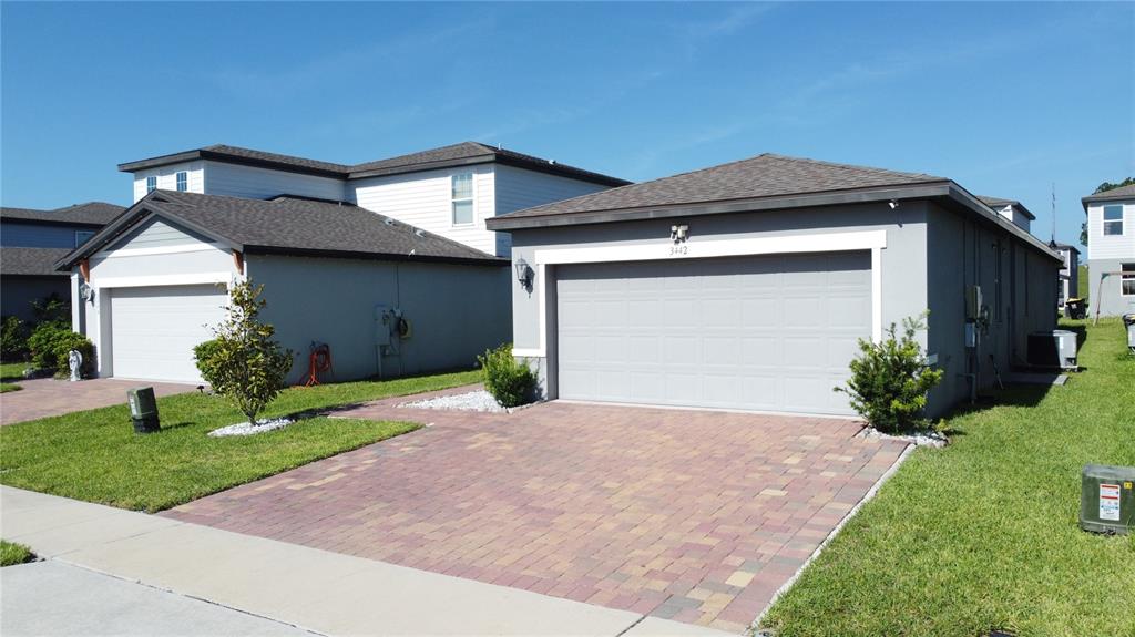 Two adjacent single-story suburban houses feature gray stucco exteriors, paver driveways, and attached garages — 3442 MONACO LN, DAVENPORT, FL