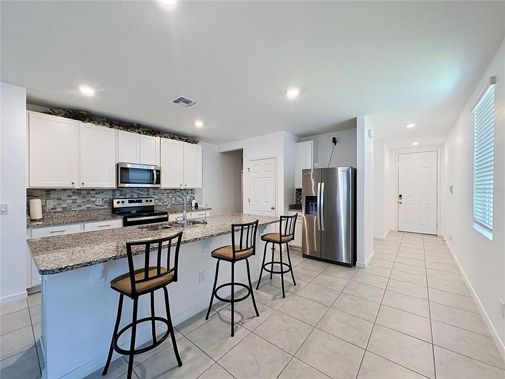 A kitchen features white cabinets, granite countertops, a stainless steel refrigerator, and a breakfast bar — 3442 MONACO LN, DAVENPORT, FL
