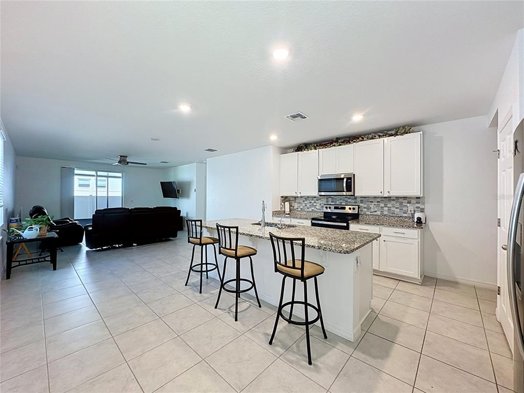 A kitchen with white cabinets, granite countertops, and an island with three bar stools — 3442 MONACO LN, DAVENPORT, FL