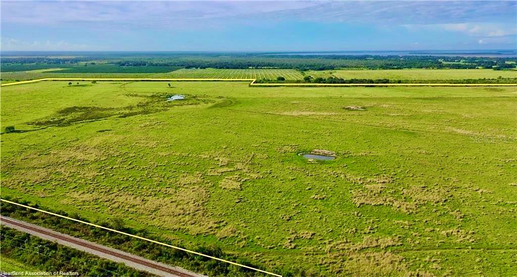 An aerial view shows a large, open grassy pasture with two small ponds and railroad tracks — 4333 US-98, LORIDA, FL