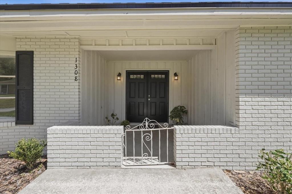 A white brick house exterior features a recessed entryway with double black doors — 1308 GLENFORD LANE, LAKELAND, FL