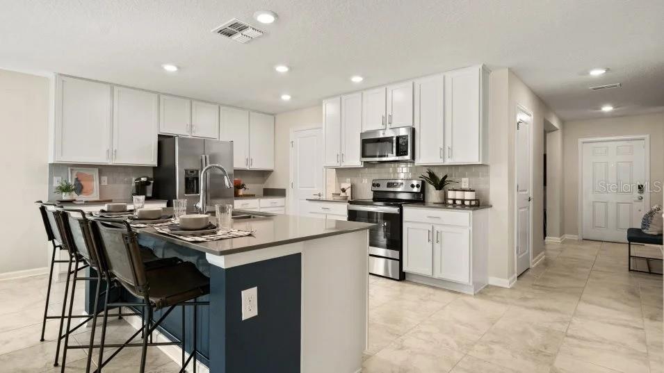 A modern kitchen features white cabinets, a dark blue island with bar seating, and stainless appliances — 2009 MYRTLE PINE STREET, KISSIMMEE, FL