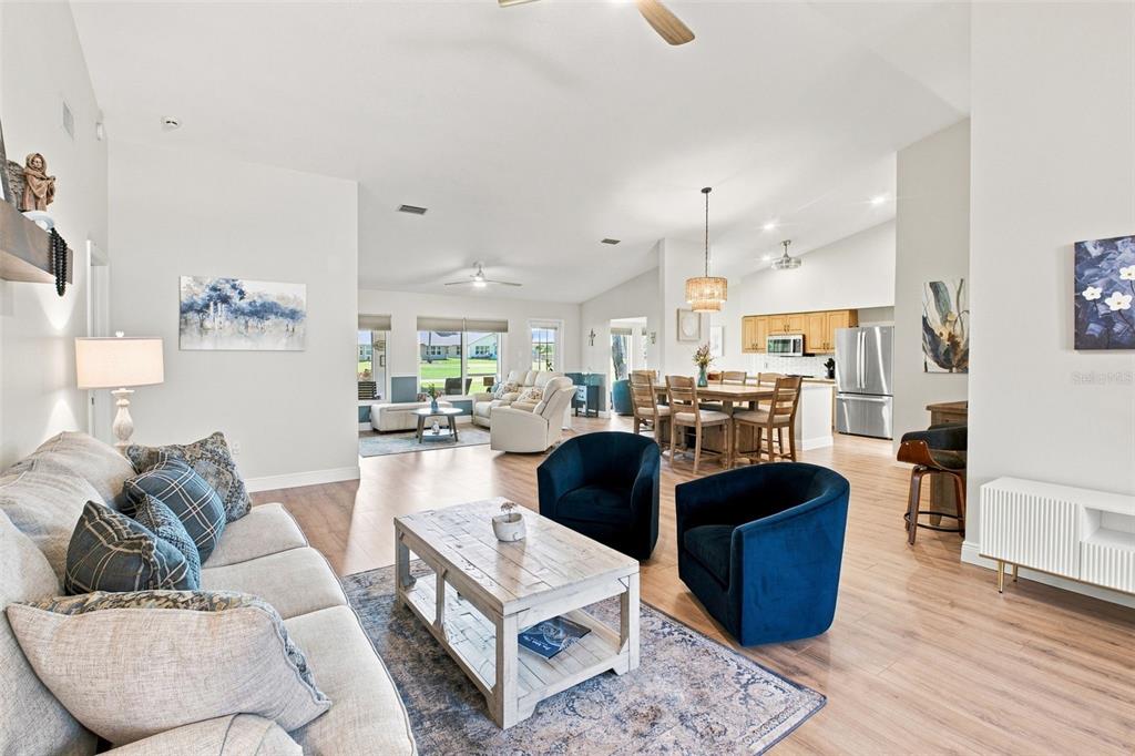 An open-concept living and dining area features light wood flooring, blue accent chairs, and kitchen — 1236 FLORA VISTA STREET, TRINITY, FL