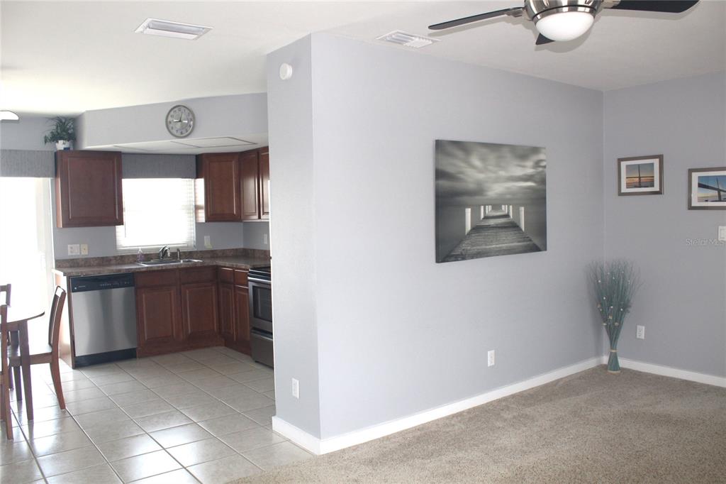 A kitchen with wood cabinets and stainless steel appliances opens to a carpeted living area — 12400 PARK BLVD UNIT 206, SEMINOLE, FL