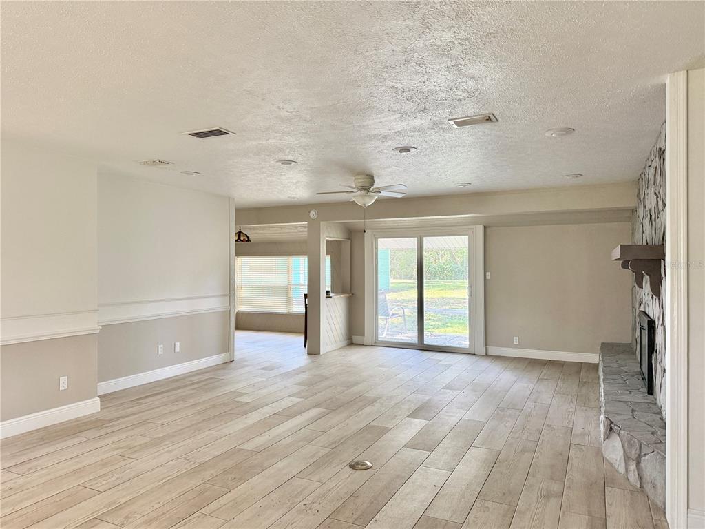 A living room with light wood-look tile flooring, a stone fireplace, and sliding glass doors — 9628 DAVIS ROAD, TAMPA, FL