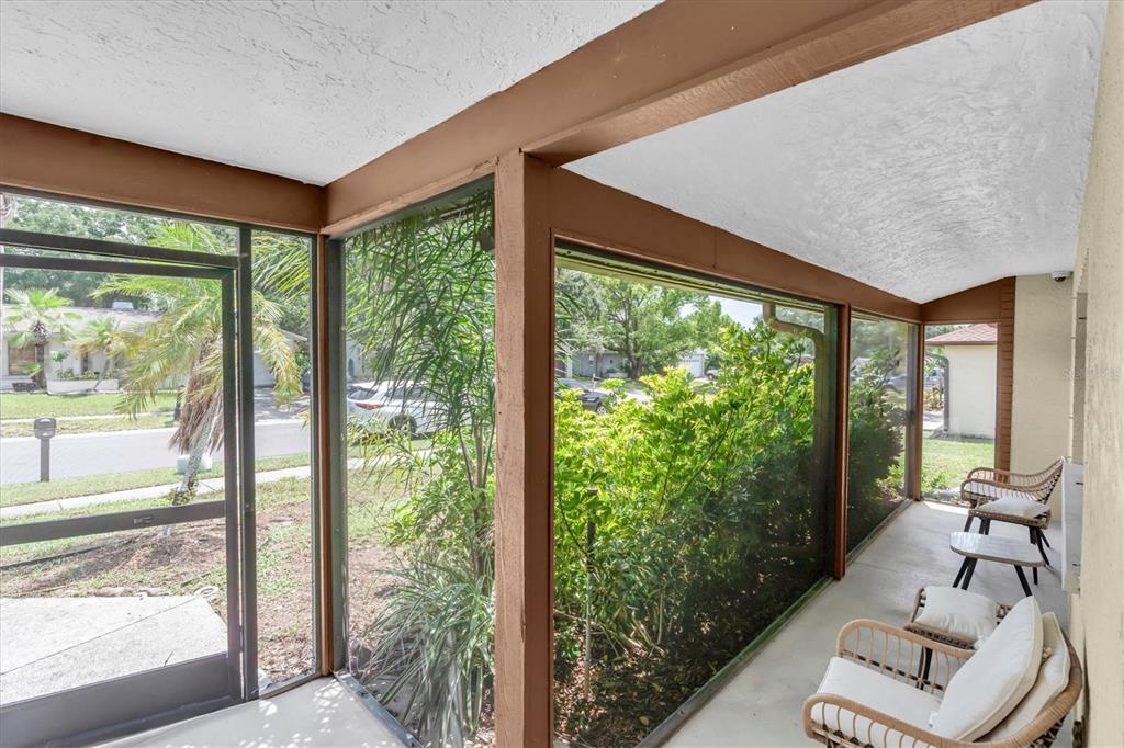 A screened-in porch features a concrete floor, wooden framing, and outdoor seating — 914 HARBOR CIRCLE, PALM HARBOR, FL