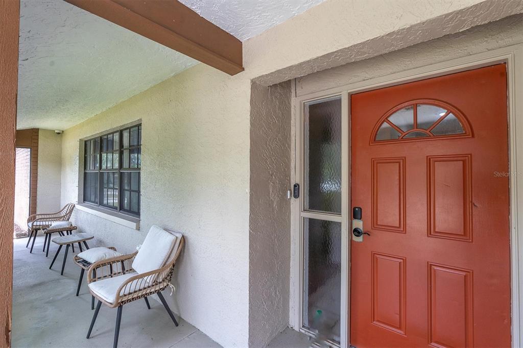 A covered porch features a red front door, a window, and two wicker chairs — 914 HARBOR CIRCLE, PALM HARBOR, FL