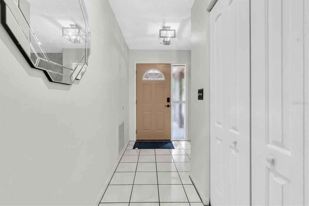 A bright entryway features white tile flooring, a tan front door, and a wall-mounted mirror — 914 HARBOR CIRCLE, PALM HARBOR, FL