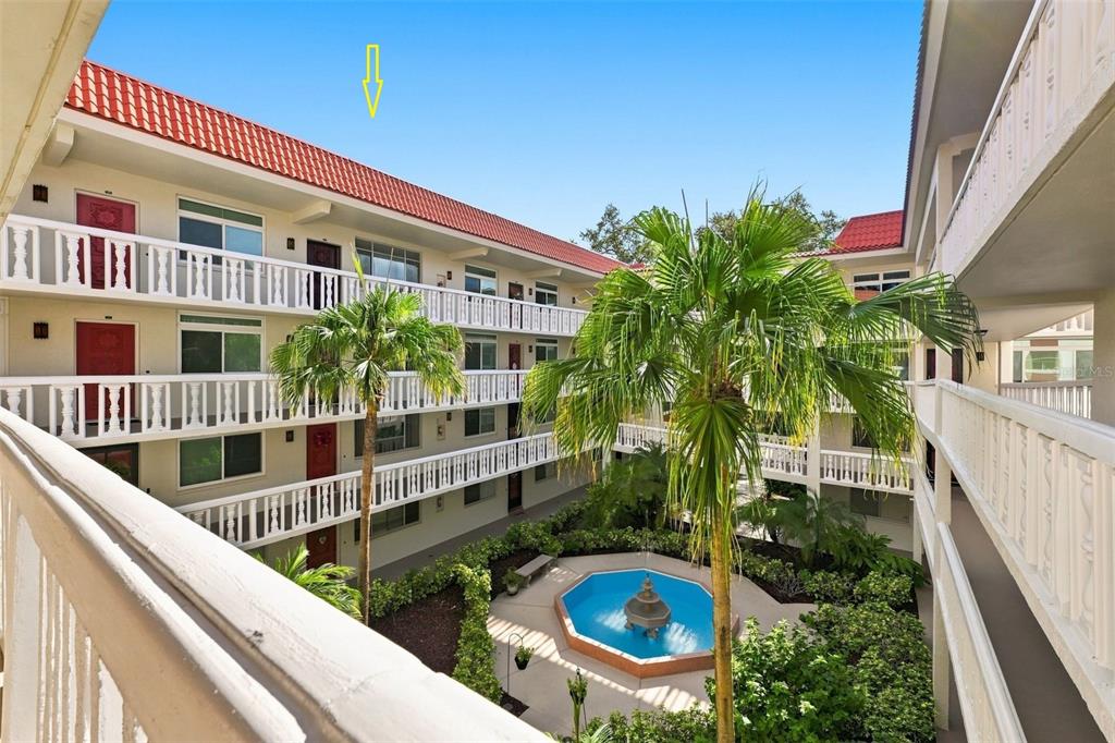 An exterior view of a multi-story apartment complex courtyard featuring a fountain and palm trees — 2650 PEARCE DRIVE UNIT 309, CLEARWATER, FL