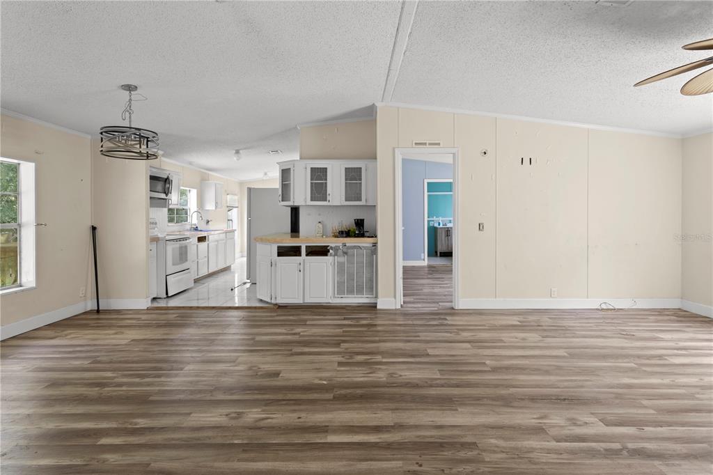 A spacious living area with wood-look flooring leads into a kitchen with white cabinetry — 24027 NW 183RD AVENUE, HIGH SPRINGS, FL