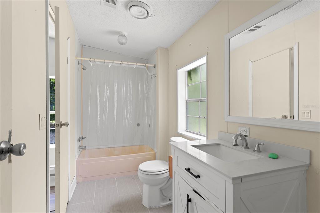 A bathroom features a white vanity, a toilet, and a pink bathtub with a shower curtain — 24027 NW 183RD AVENUE, HIGH SPRINGS, FL