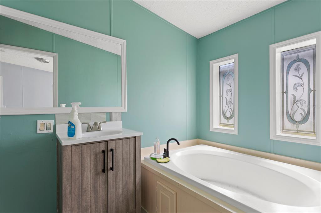 A bathroom features a wood vanity, a soaking tub, and two stained-glass windows — 24027 NW 183RD AVENUE, HIGH SPRINGS, FL
