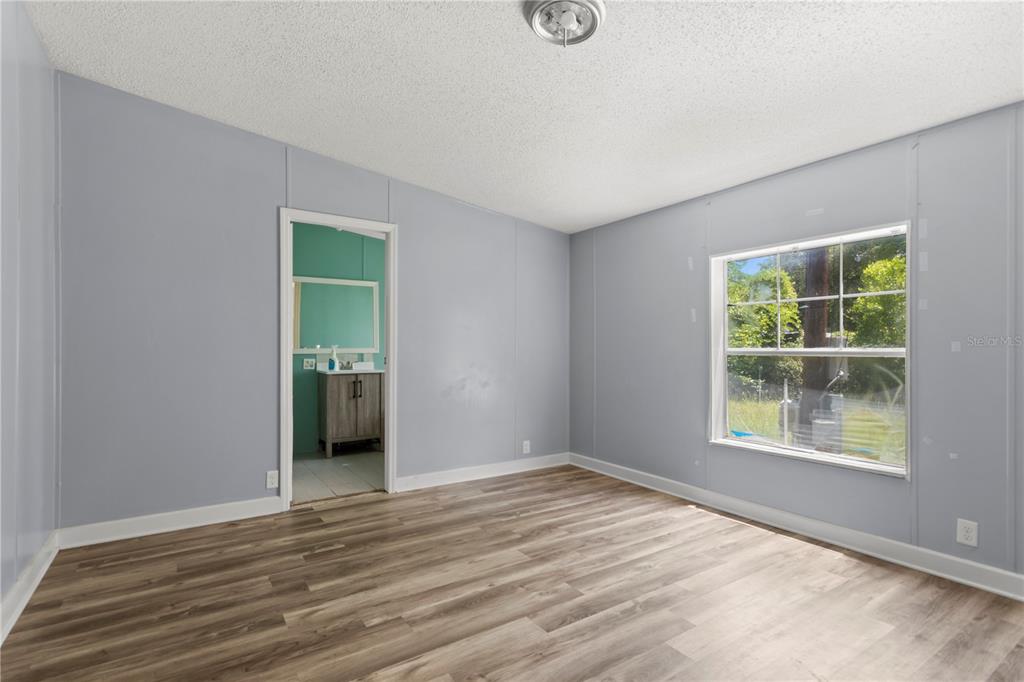 A bedroom with light gray walls, wood-look flooring, and an attached bathroom — 24027 NW 183RD AVENUE, HIGH SPRINGS, FL