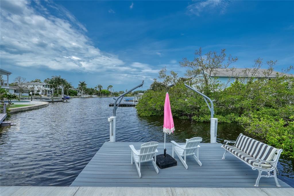 A wooden dock features two white chairs, a pink umbrella, and a striped metal bench — 223 PINECREST DRIVE, PALM HARBOR, FL