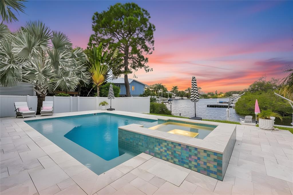 A swimming pool and spa with blue tile accents overlook a canal at sunset — 223 PINECREST DRIVE, PALM HARBOR, FL