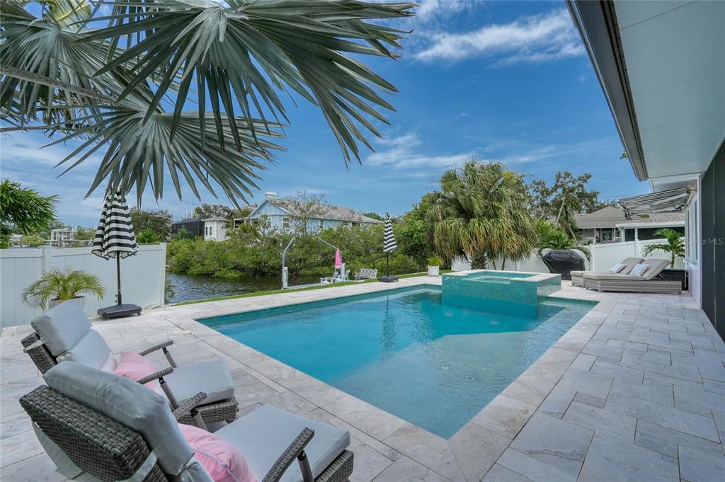 A backyard swimming pool with a built-in spa and stone patio overlooking a canal — 223 PINECREST DRIVE, PALM HARBOR, FL
