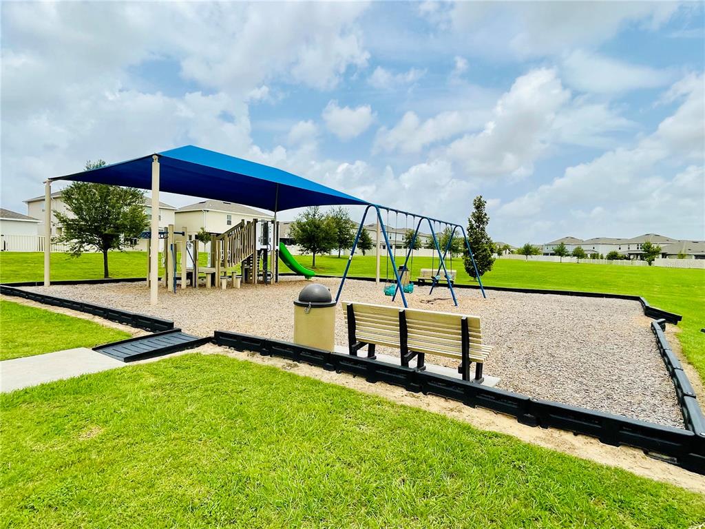 A playground with a blue shade canopy, swing set, and slide on a gravel surface — 436 LEMONGRASS ROAD, MINNEOLA, FL