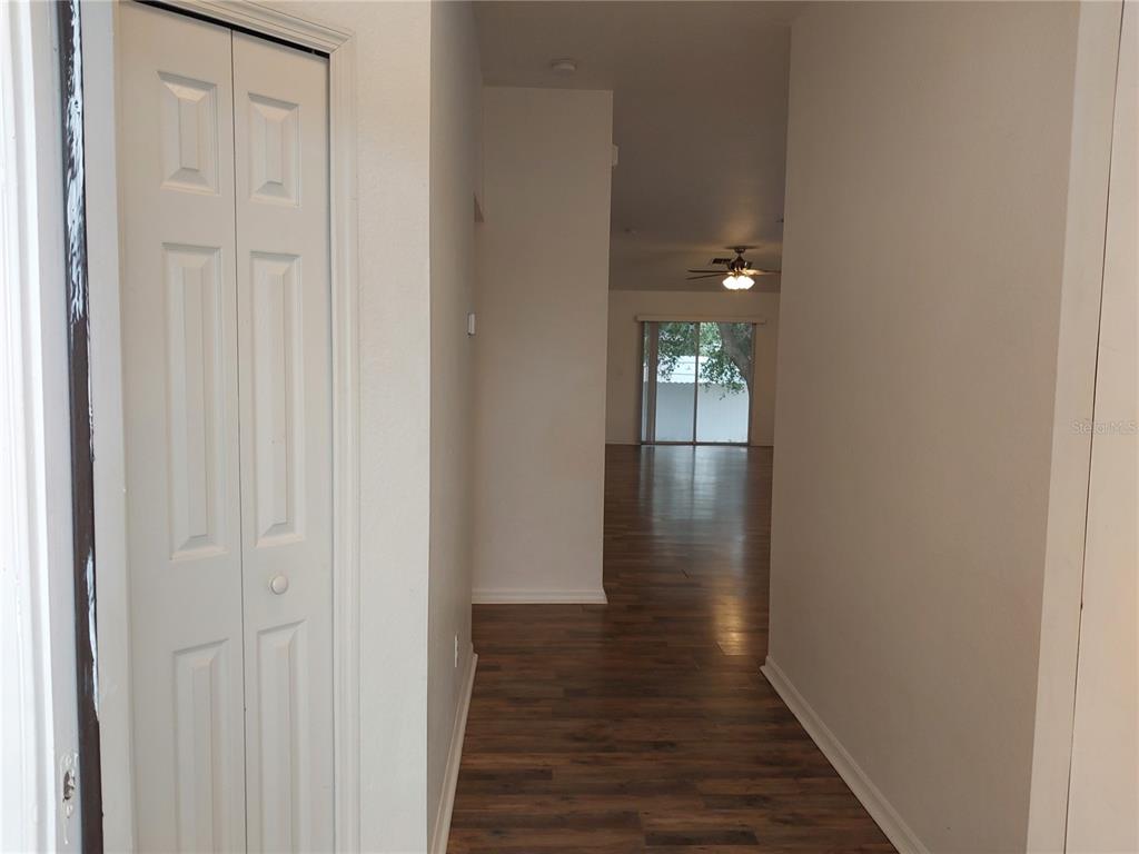 A hallway with wood-look flooring leads to an open living area with sliding glass doors — 557 WINDERMERE DRIVE, LEHIGH ACRES, FL