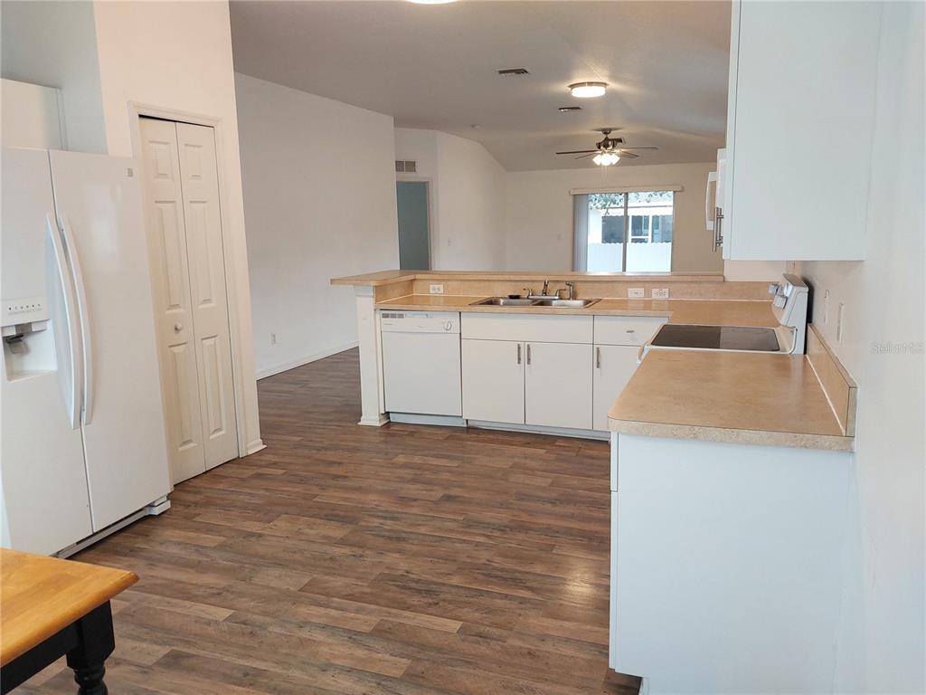 A kitchen with white cabinets, tan countertops, and wood-look flooring opens to a living area — 557 WINDERMERE DRIVE, LEHIGH ACRES, FL
