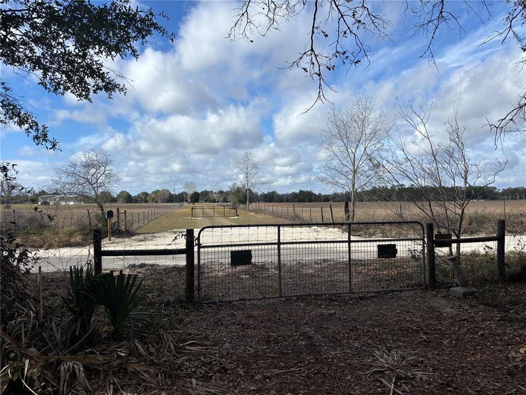 A metal gate opens onto a dirt driveway leading through a large, fenced-in grassy field — 31 SE 190TH AVENUE, OLD TOWN, FL