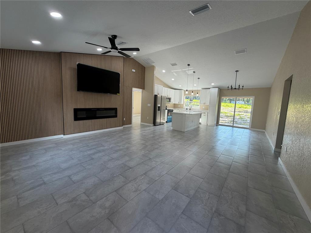 An open-concept living room and kitchen featuring wood-slat wall paneling, tile flooring, and vaulted ceilings — 13268 SE 44TH CT, BELLEVIEW, FL