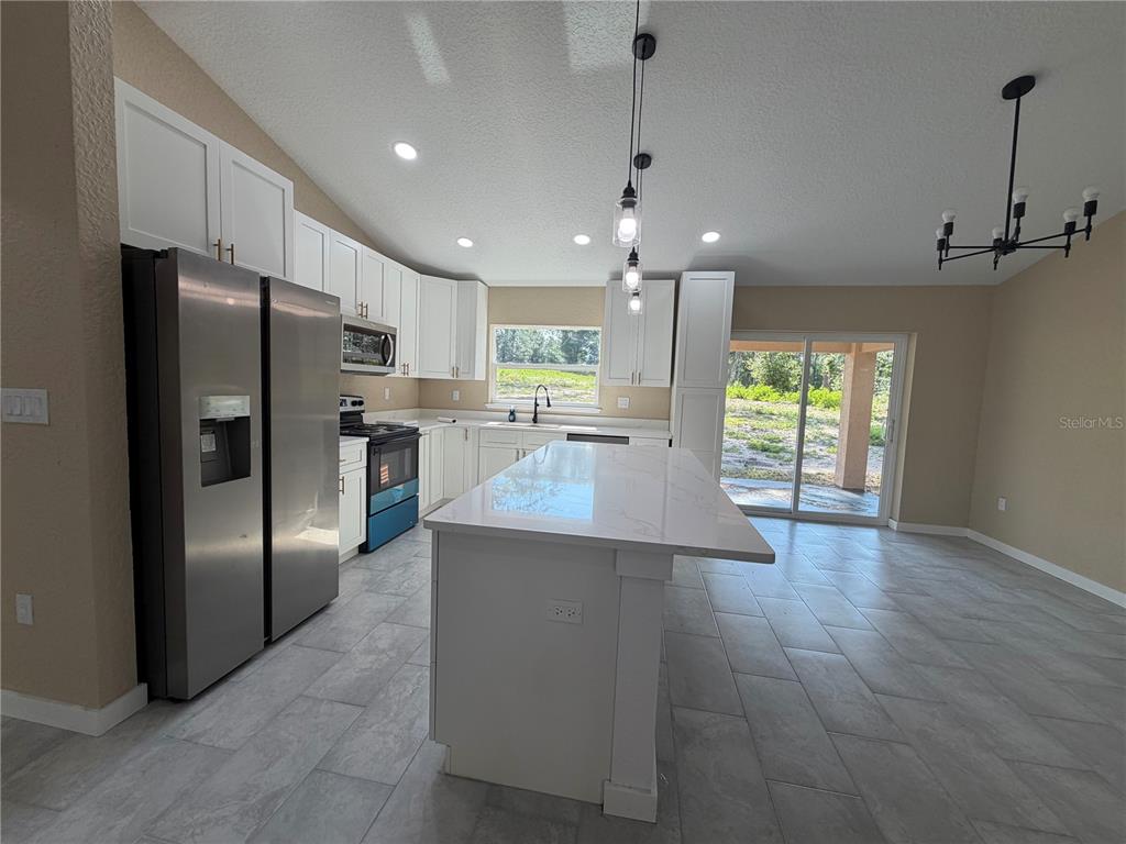 A kitchen features white cabinets, stainless steel appliances, a quartz island, and tile flooring — 13268 SE 44TH CT, BELLEVIEW, FL