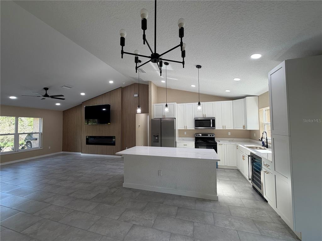 An open-concept kitchen and living area features white cabinetry, a central island, and wood-paneled walls — 13268 SE 44TH CT, BELLEVIEW, FL