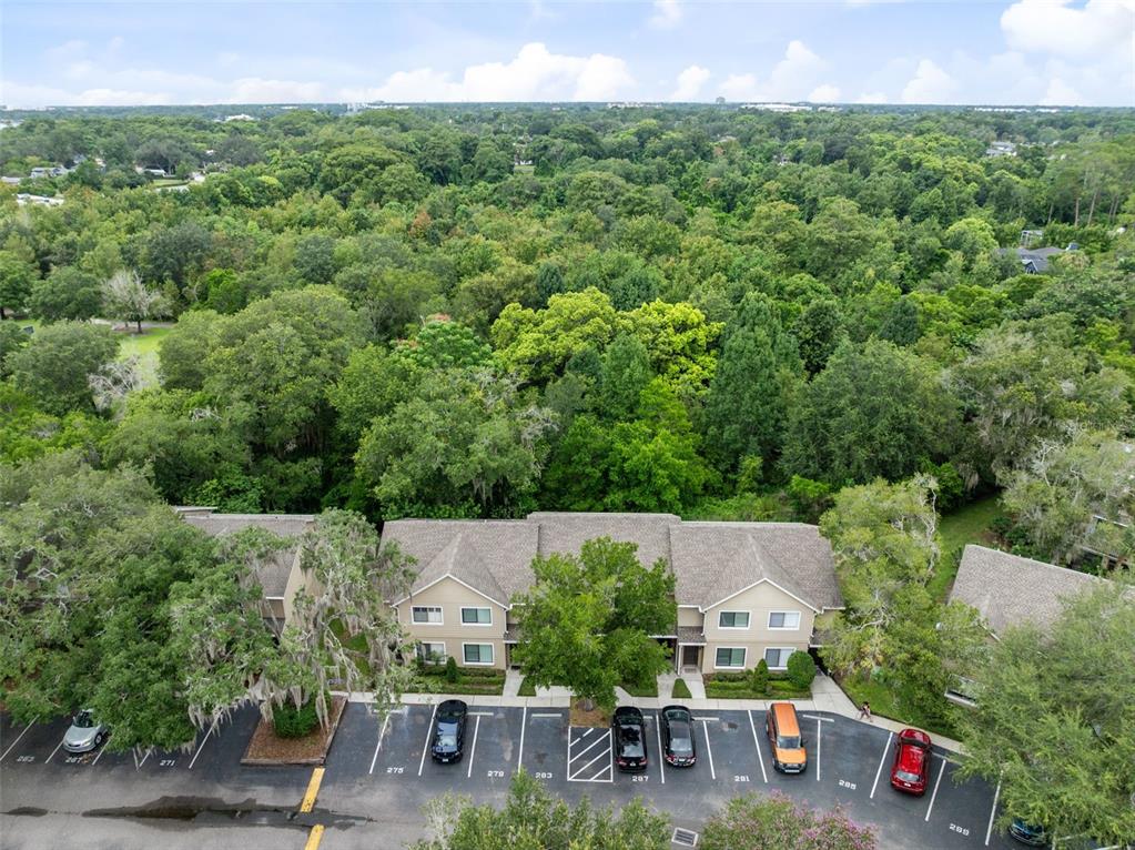 An aerial view shows a two-story apartment building with a parking lot and surrounding forest — 283 SANDLEWOOD TRAIL UNIT 3, WINTER PARK, FL