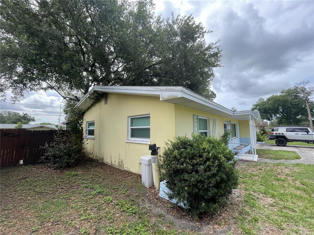 The exterior of a yellow, single-story house features a large tree and a parked vehicle — 635 DEVILLE DRIVE E, LARGO, FL