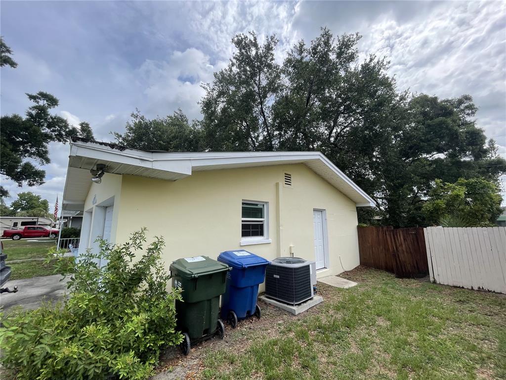 The exterior of a yellow detached garage features two trash bins and an air conditioning unit — 635 DEVILLE DRIVE E, LARGO, FL