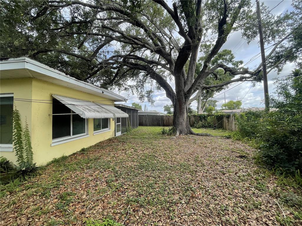 A yellow house exterior features a metal awning over windows and a large oak tree — 635 DEVILLE DRIVE E, LARGO, FL