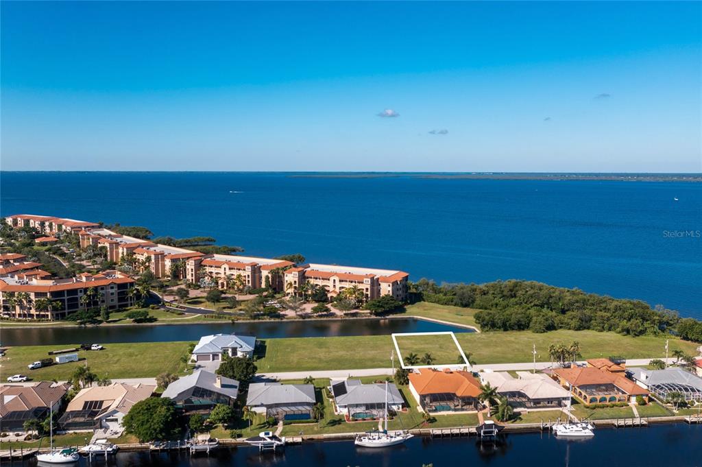 An aerial view shows a vacant waterfront lot situated between residential homes and a bay — 65 COLONY POINT DRIVE, PUNTA GORDA, FL