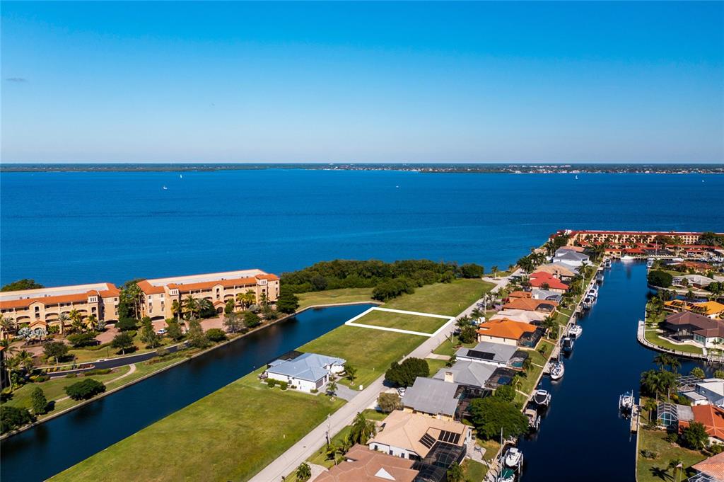 An aerial view shows a vacant waterfront lot situated between residential homes and a canal — 65 COLONY POINT DRIVE, PUNTA GORDA, FL