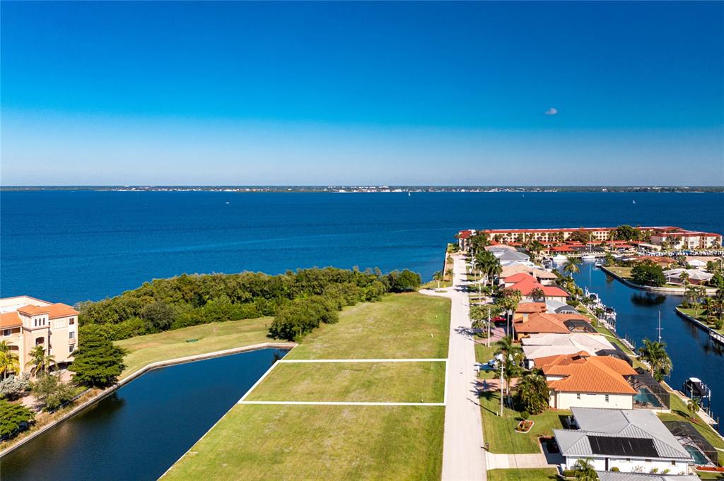 An aerial view shows a vacant waterfront lot next to a residential street and canal — 65 COLONY POINT DRIVE, PUNTA GORDA, FL