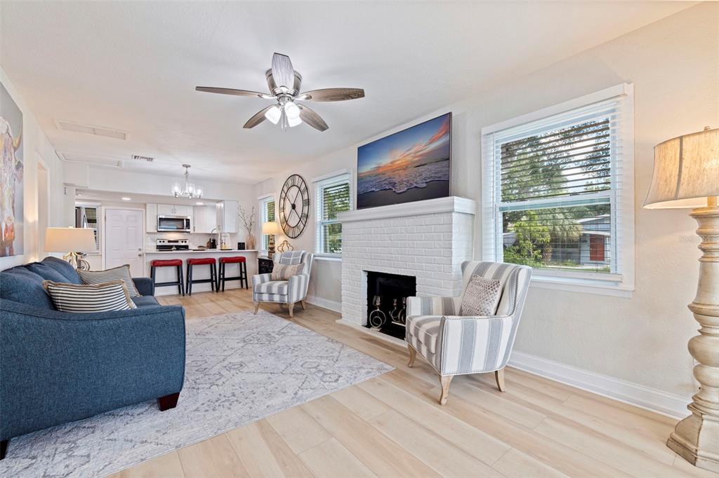 A living room with a white brick fireplace, blue sofa, striped chairs, and open kitchen — 1601 54TH STREET S, GULFPORT, FL