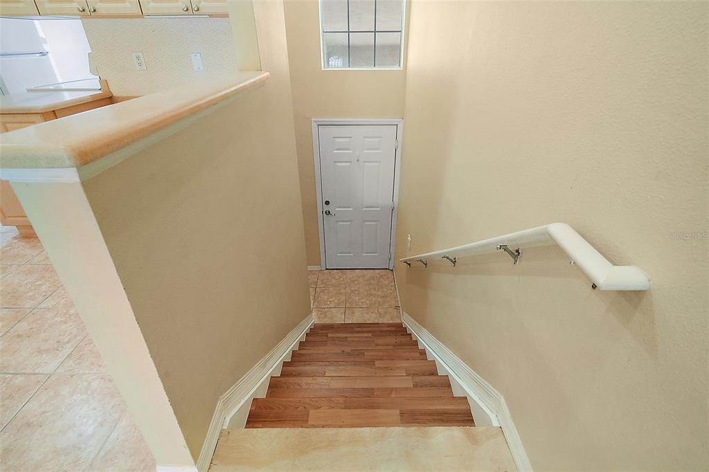 A staircase with wood-look steps leads down to a white door and tiled landing — 5368 COMPASS POINT UNIT 202, OXFORD, FL