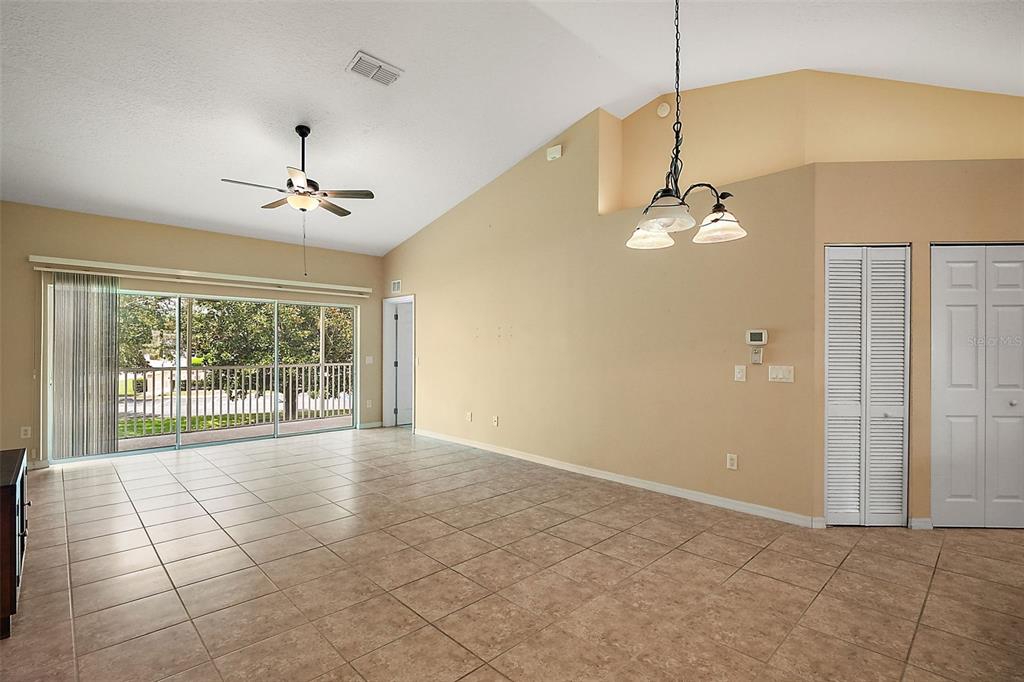 A living room with beige tile flooring, vaulted ceilings, a ceiling fan, and sliding glass doors — 5368 COMPASS POINT UNIT 202, OXFORD, FL