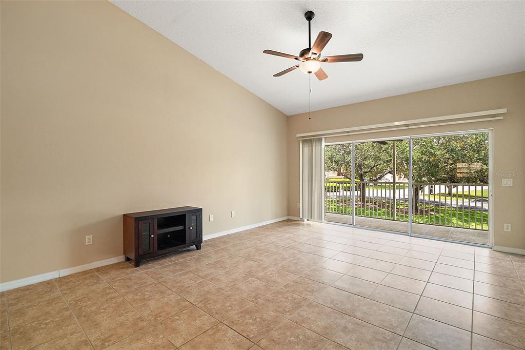 A living room with beige walls, tile flooring, a ceiling fan, and sliding glass doors — 5368 COMPASS POINT UNIT 202, OXFORD, FL