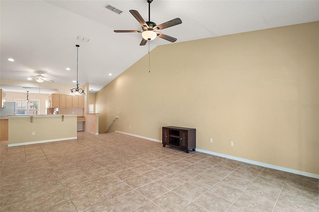 A living room with vaulted ceilings, tile flooring, and a dark wood media console — 5368 COMPASS POINT UNIT 202, OXFORD, FL