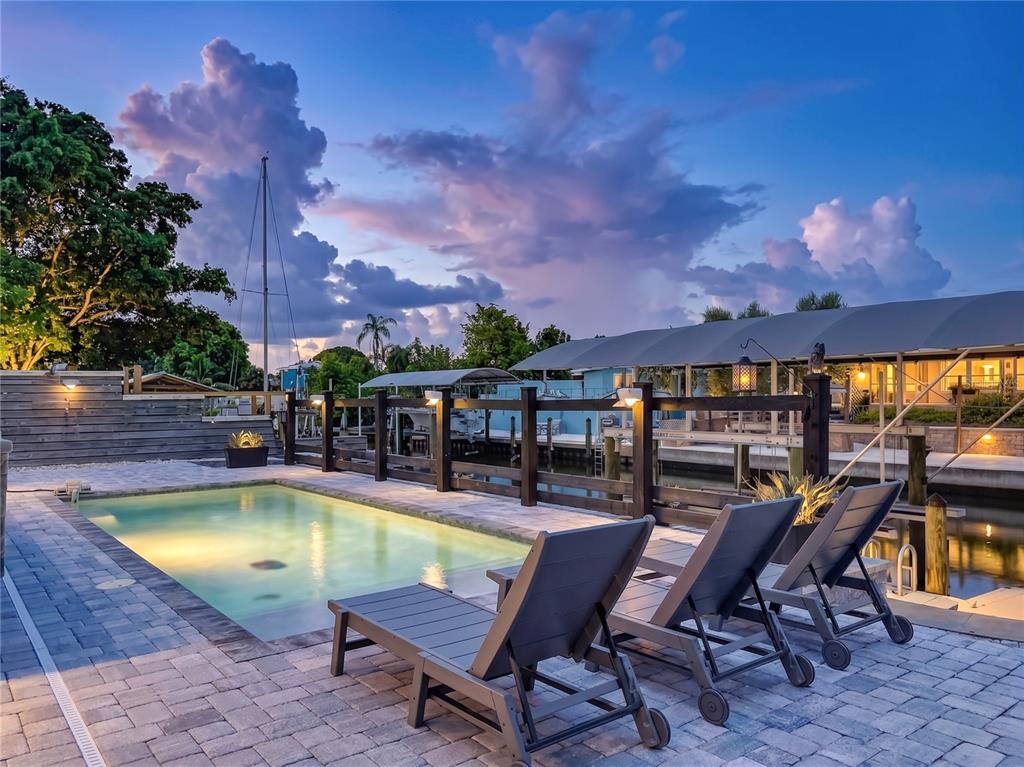 A swimming pool and lounge chairs sit on a paved patio overlooking a boat dock — 6835 GEORGIA AVENUE, BRADENTON, FL
